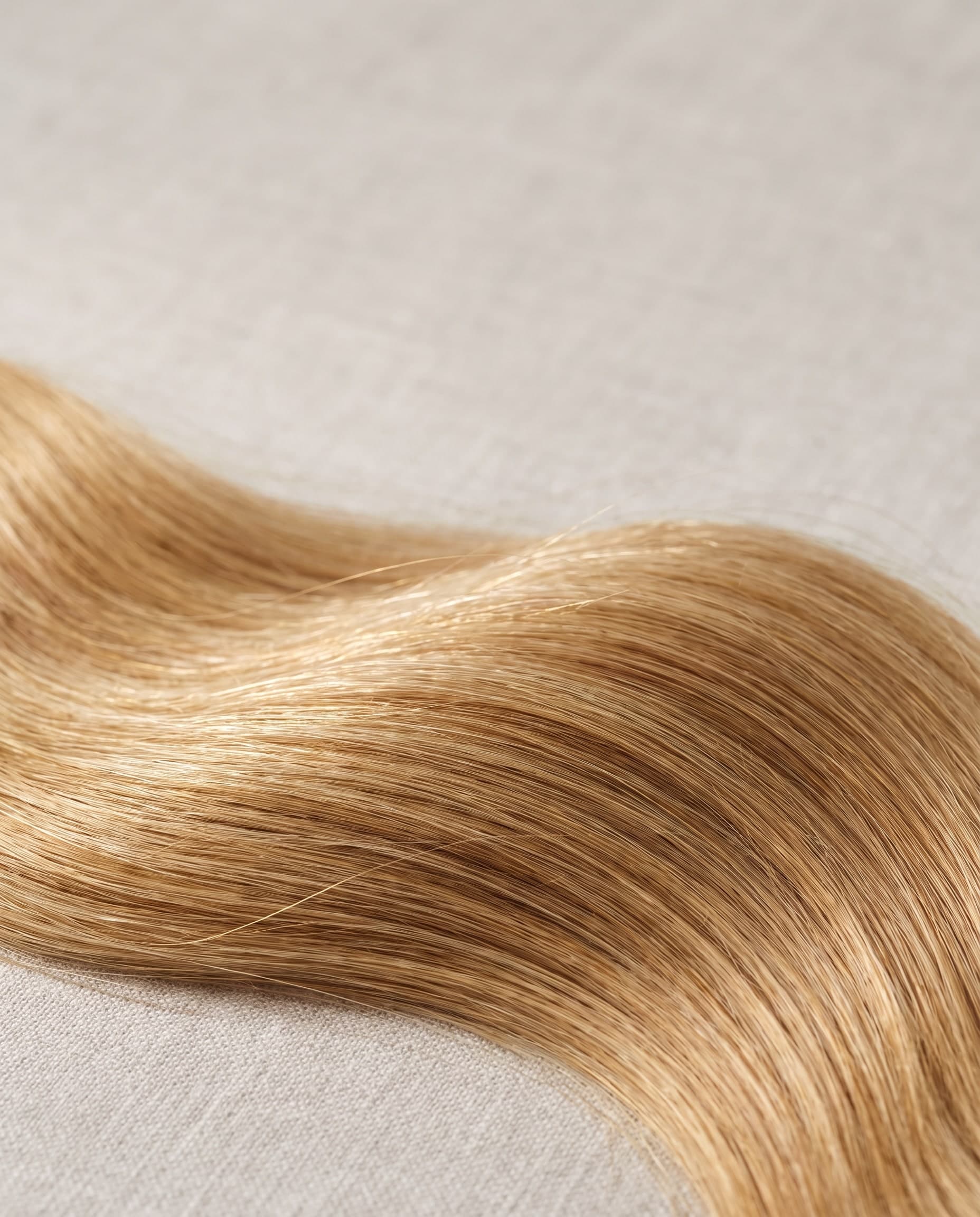 Honigblonde, leicht gewellte Haarsträhnen auf hellem Leinen
